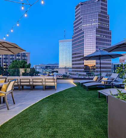 a rooftop terrace with tables and umbrellas and a city in the background