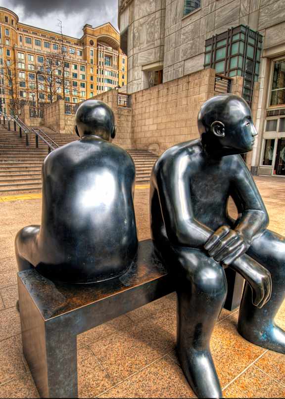 Two black sculptures of people sitting on a bench.