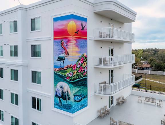 A mural on a building shows a sunset with a bird flying and a fish swimming.