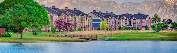 A serene lake in front of a mountain range with a building in the foreground.