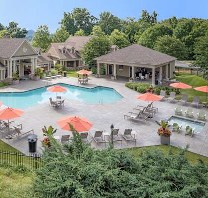 A large outdoor swimming pool surrounded by red umbrellas and lounge chairs.