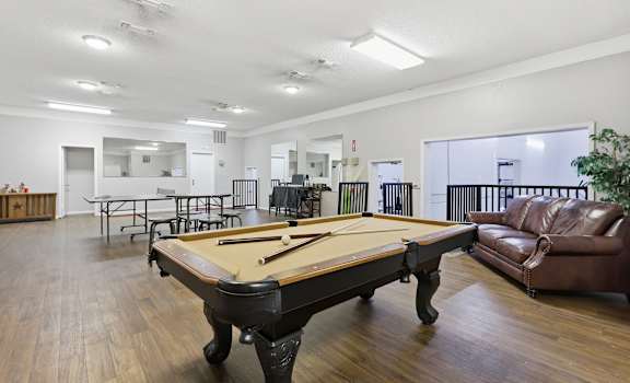 A pool table is in the middle of a room with a couch and chairs.