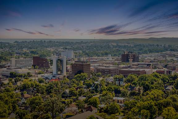 Rapid City A cityscape with buildings and trees under a blue sky with clouds.