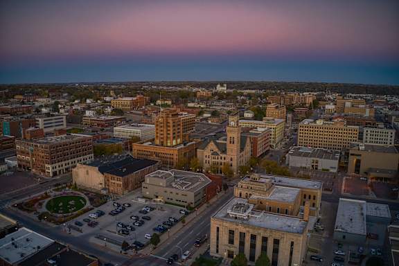 Sioux City A cityscape with buildings and a parking lot is captured during sunset.