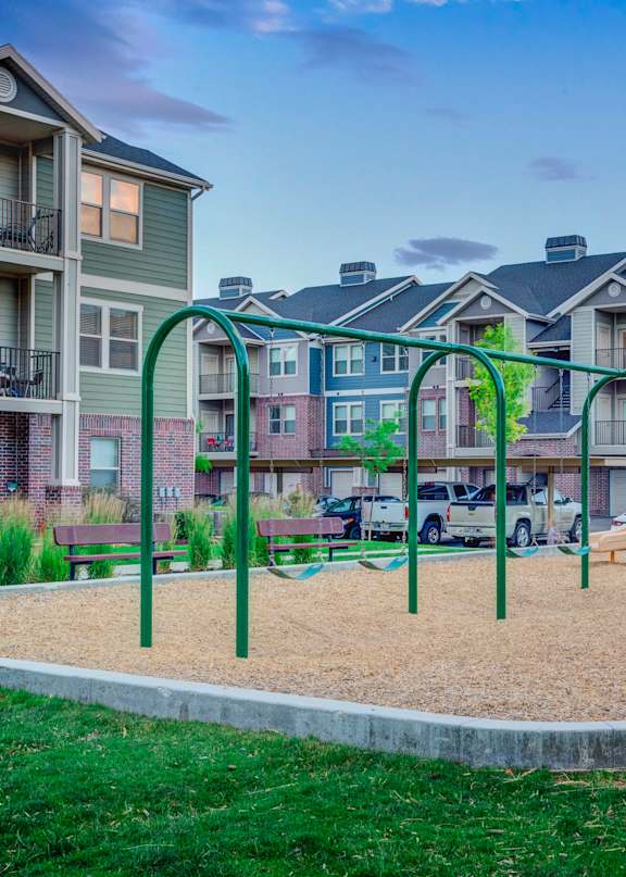 A playground with a slide, swings, and a sandbox in the foreground, surrounded by apartment buildings.