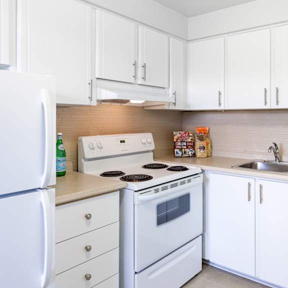 A white kitchen with a stove, sink, and refrigerator.