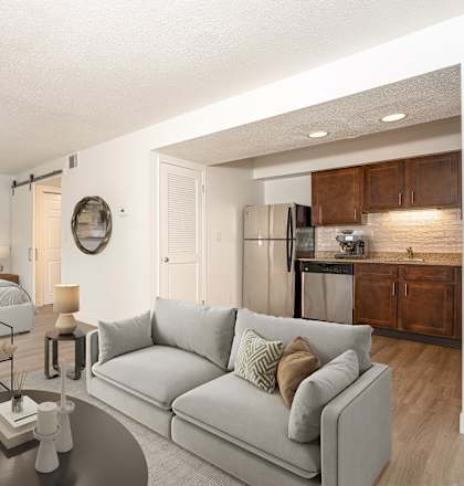 A modern living room with a grey couch and a bed in the background.