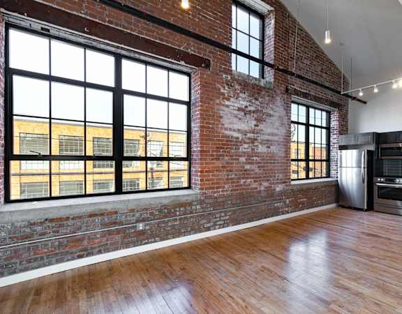 A large empty room with wooden floors and a brick wall.