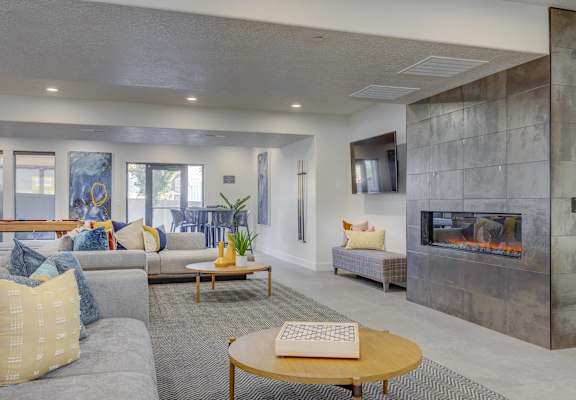 A modern living room with a grey couch, a yellow pillow, a wooden coffee table, a fireplace, and a grey wall.