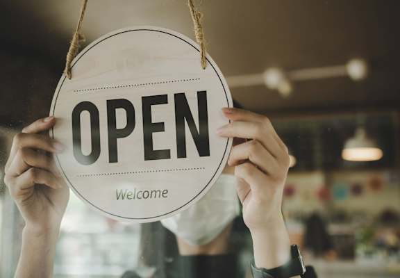 a person holding an open sign in a store window