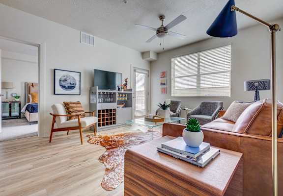 A living room with a brown couch, a wooden chair, a glass coffee table, and a ceiling fan.