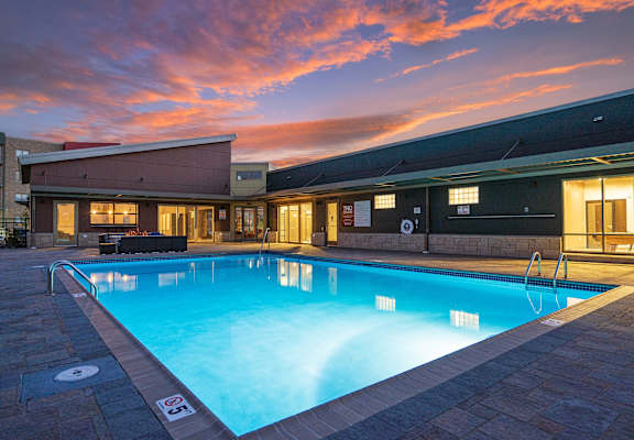 A swimming pool in front of a building with a sunset sky in the background.