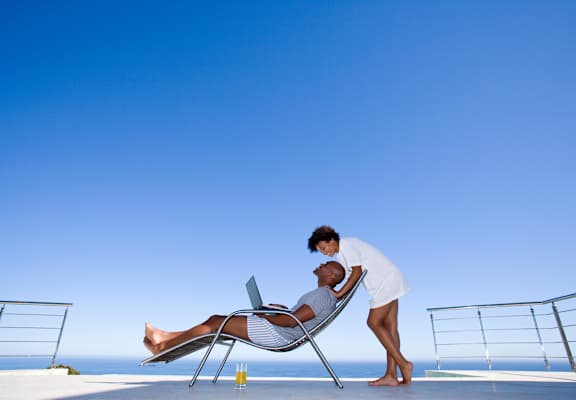 a woman standing next to a man sitting in a chair with a laptop
