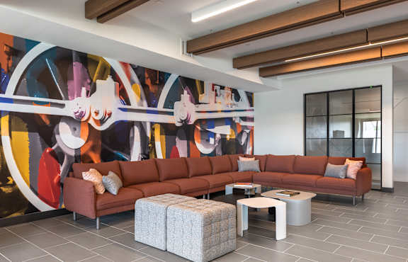 A living room with a large mural on the wall and a brown sofa.
