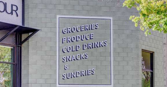 a sign on the side of a building that says groceries produce cold drinks snacks and sundries