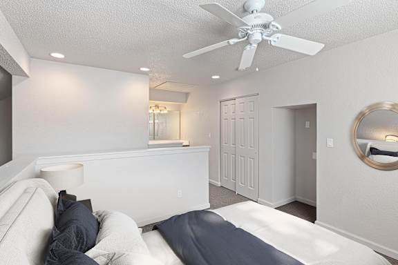A white bedroom with a bed, a ceiling fan, and a mirror on the wall.