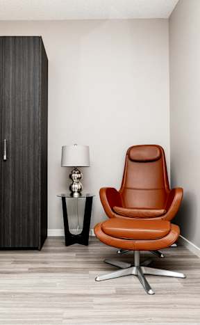 A brown leather chair sits in front of a tall cabinet in a room with a wooden floor.