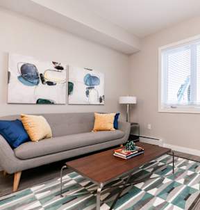 A living room with a grey couch, a coffee table, a chair, and a painting on the wall.