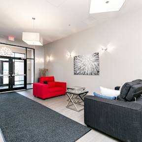 A black couch sits in a white room with a red chair and a glass door.