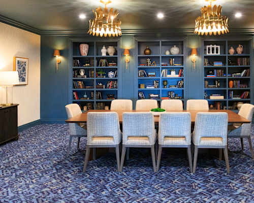 A room with a long table and chairs with a bookshelf in the background.