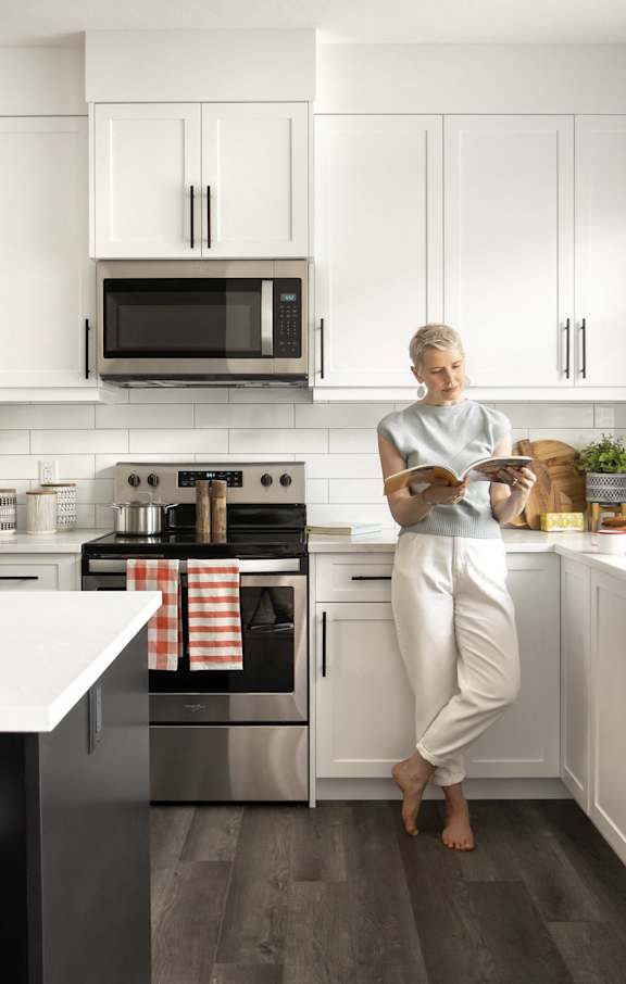 A woman is standing in a modern kitchen with white cabinets and stainless steel appliances.