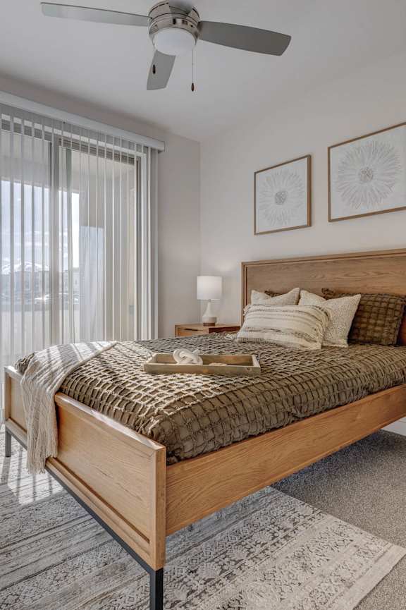 A bedroom with a large bed, a ceiling fan, and a window with blinds.