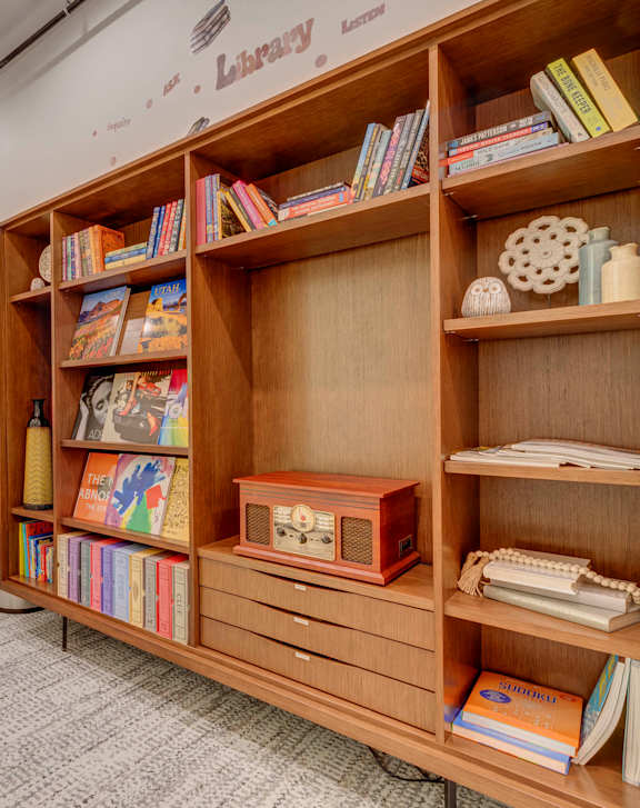 A room with a bookshelf, chairs, and a carpet.