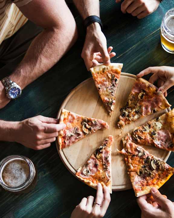 A group of people sharing a pizza and beer at a table.