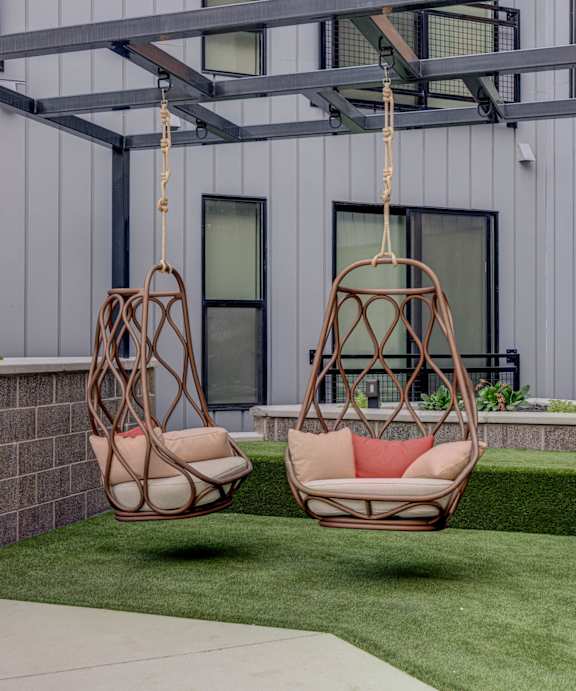 Two hanging chairs are suspended from a metal frame in a backyard.