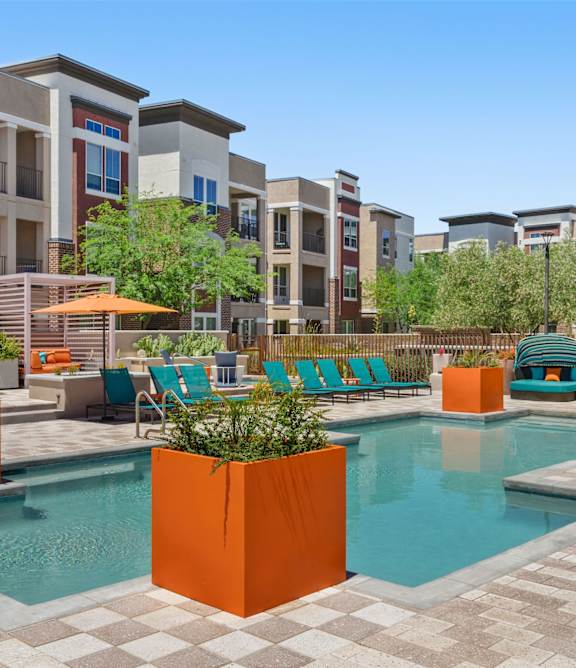 A pool surrounded by orange planters and chairs.