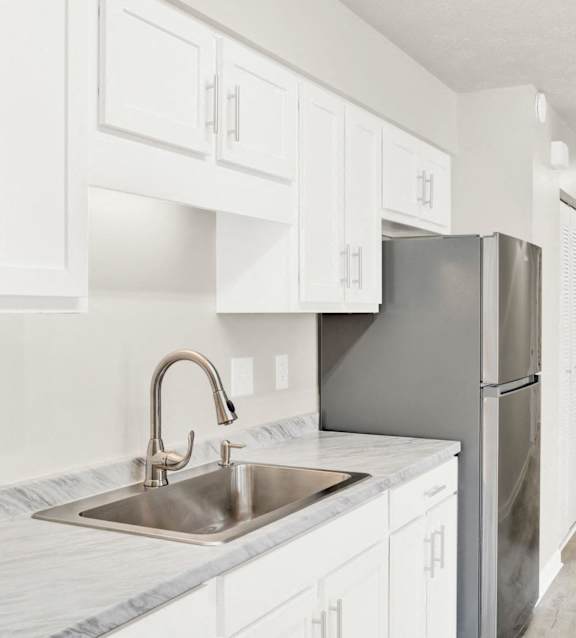 a white kitchen with a stainless steel refrigerator and sink