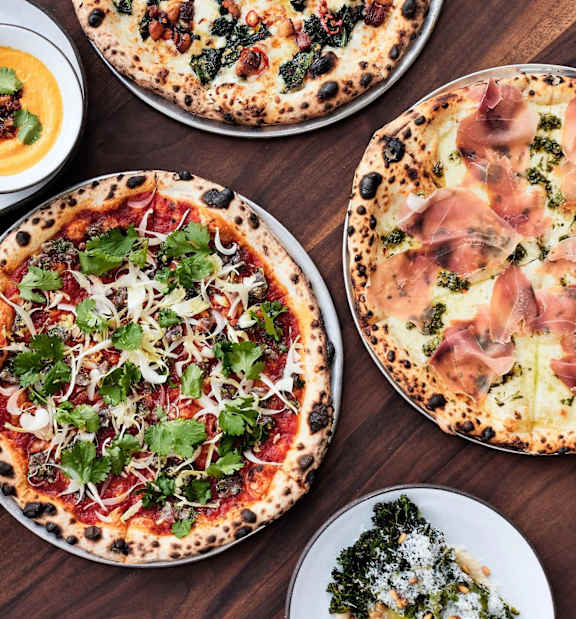A table with several pizzas and side dishes.