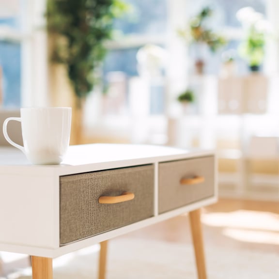 A white coffee table with a cup on top and two drawers is in front of a couch.