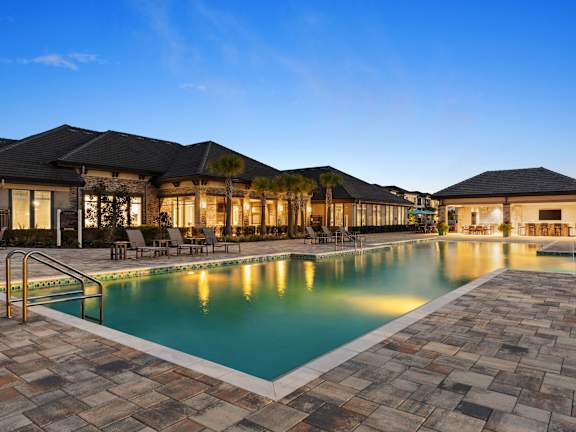 A large outdoor swimming pool surrounded by a stone patio and a building with a black roof.