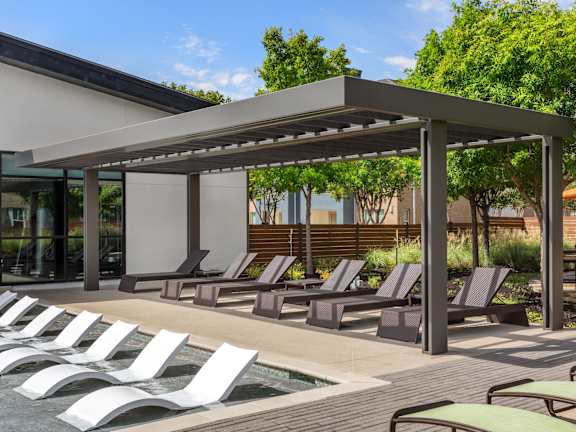 A row of sun loungers are arranged on a wooden deck next to a pool.