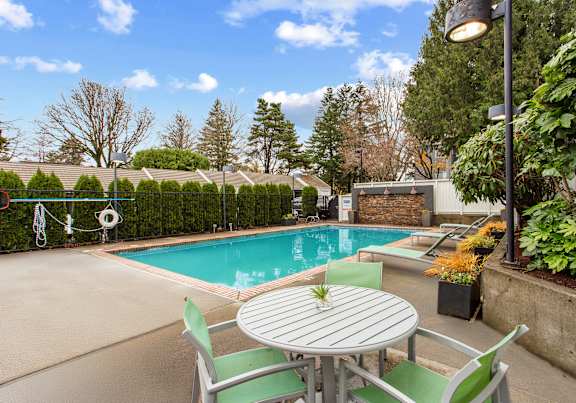 A table with a plant on it sits in front of a pool.