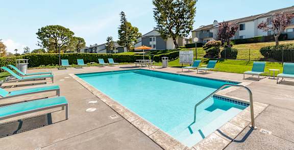 A black fence surrounds a grassy area with a pool and houses in the background at Chaparral Apartments , California 93551
