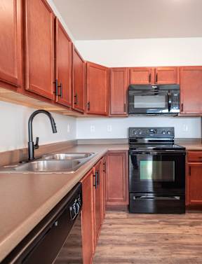 A kitchen with black appliances and wooden cabinets at Meadowlark Place Apartments, Grimes, Iowa