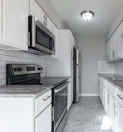 A kitchen with white cabinets and a black and white tiled backsplash.