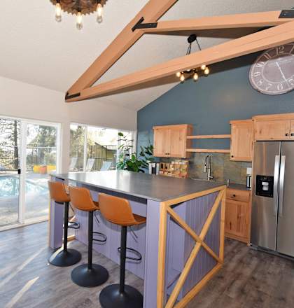 A kitchen with a purple wall and a bar area with stools.