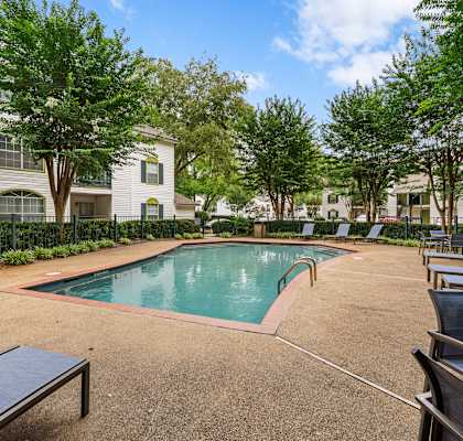 A pool surrounded by trees and chairs.