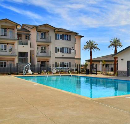 A swimming pool in front of a building with a fence and palm trees.