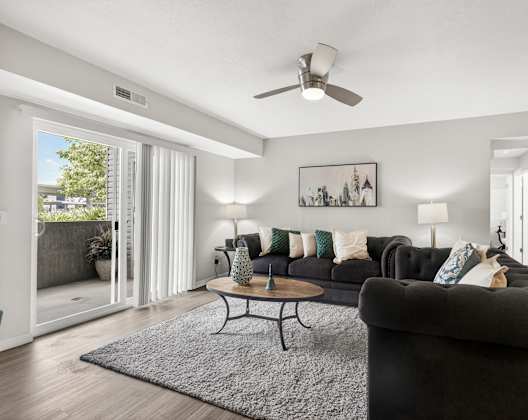 A living room with a black couch and a ceiling fan.