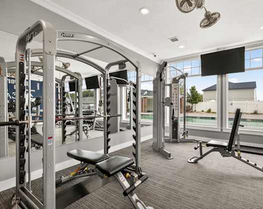 A gym with a row of machines and a window showing a building and trees.