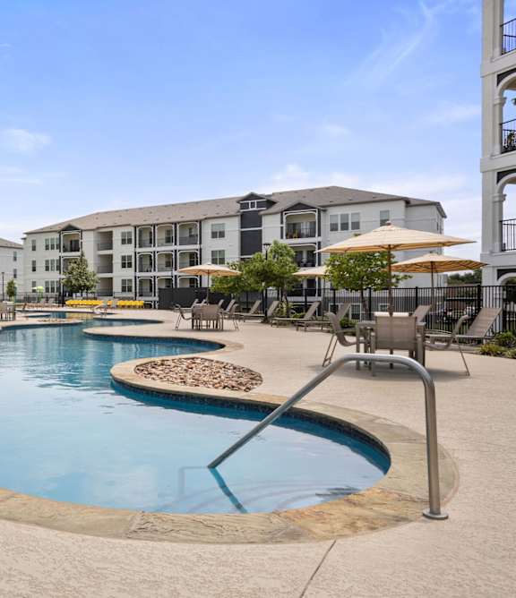 A large outdoor swimming pool surrounded by a concrete patio and chairs.