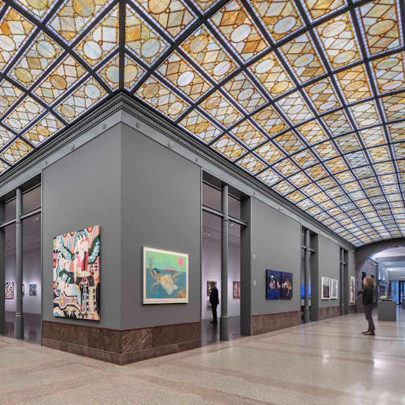 A group of people are walking through a hallway with art on the walls.