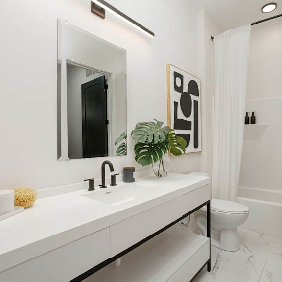 A white bathroom with a sink, mirror, toilet, and a plant. at Vintage Edge Nashville Apartments, Tennessee, 37211