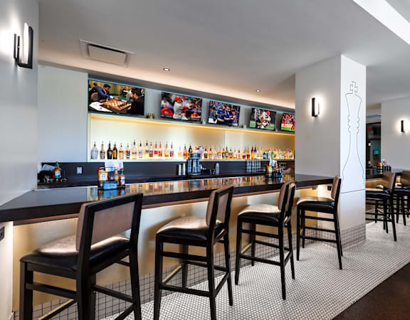 A bar with black chairs and a counter with bottles on it at Clayton on the Park Apartments, Clayton, Missouri