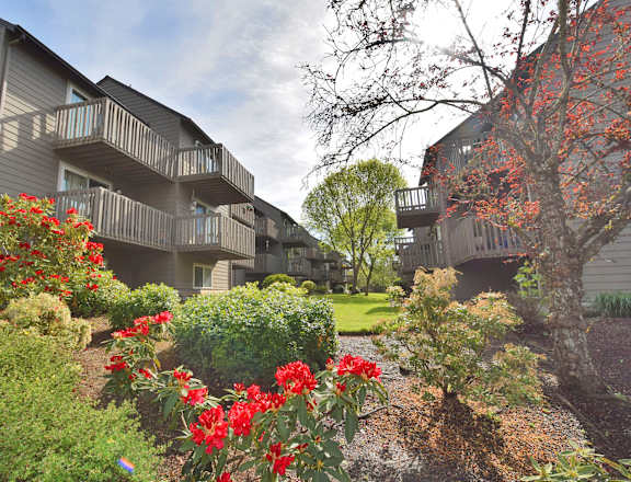 a landscaped yard with red flowers in front of apartment buildings