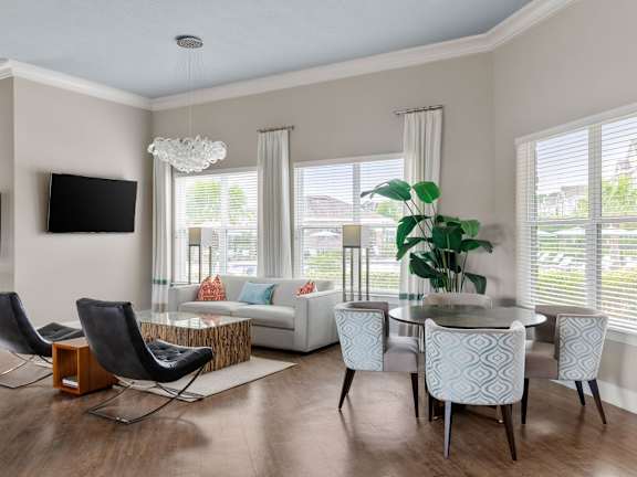 A modern living room with a white sofa, a glass coffee table, and a TV mounted on the wall.